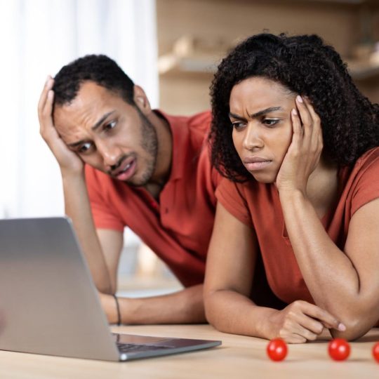 A couple sitting on a couch, one visibly tired while the other offers support