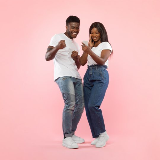 Couple sharing a laugh while looking at a smartphone, symbolizing modern digital connection and love in the 21st century.